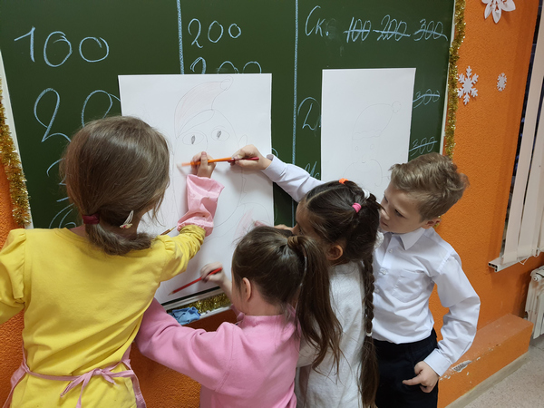 Дети на листе бумаги рисуют совместный рисунок Деда Мороза