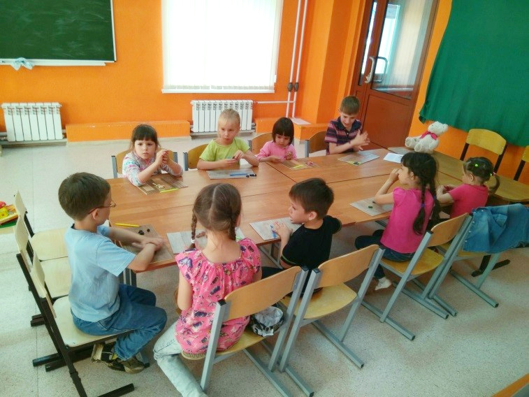 Дети сидят за столом с альбомами и карандашами