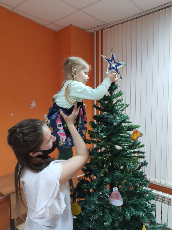 Девушка и маленькая девочка надевают звезду на ёлку